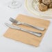 A fork and knife on a Creative Converting Glittering Gold luncheon napkin next to a plate of food.