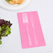 A fork and knife on a pink Creative Converting guest towel next to a plate of salad.