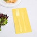 A fork and knife on a yellow Creative Converting guest towel next to a plate of salad.