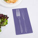 A purple Creative Converting guest towel with a fork and knife on it next to a plate of salad.