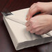 A person wrapping a Creative Converting ivory luncheon napkin around a fork.