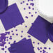 A purple luncheon napkin with confetti on a table with purple plates.