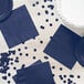 A navy blue Creative Converting luncheon napkin on a table set with navy blue paper plates.