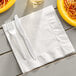 A white 1/4 fold luncheon napkin with a fork and knife on a table.