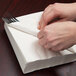 A person's hands wrapping a white luncheon napkin around a fork.