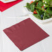 A plate of salad with a burgundy luncheon napkin and a fork.