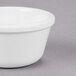 A close-up of a Carlisle white melamine ramekin on a gray surface.