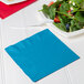 A turquoise blue Creative Converting luncheon napkin with a plate of salad and a fork.