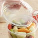 A hand holding a Choice translucent plastic deli container filled with fruit.