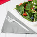 A plate of salad with a fork and a Creative Converting Shimmering Silver luncheon napkin.