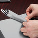 A person wrapping a fork and knife in a Shimmering Silver luncheon napkin.