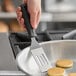 A hand holding a Tablecraft FirmGrip slotted mini turner over small pancakes.