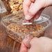 A person's hand putting a Square Recycled PET Deli Container Lid on a container of food.