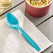 A Bermuda blue heavy weight plastic spoon on a napkin next to a bowl of noodles.