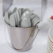 A bucket filled with Creative Converting Shimmering Silver plastic spoons.