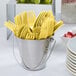 A bucket of yellow plastic forks on a table.