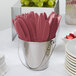 A bucket of burgundy plastic knives on a table with a stack of plates.