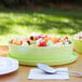 A lime melamine bowl with fruit salad on a table outdoors.