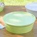 A lime green melamine bowl with a lid on a wood table.
