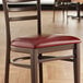 A Lancaster Table & Seating Spartan Series burgundy vinyl padded chair seat on a chair at a table in a restaurant.