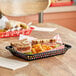 A Tablecraft black rectangular plastic fast food basket with sandwiches and fries on a table.