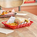 A red Tablecraft rectangular plastic fast food basket with a sandwich and fries on a table.