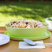 A bowl of pasta with olives and spices in a lime melamine bowl on a table.
