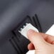 A hand pressing a white button on a black San Jamar Twin Classic toilet paper dispenser.