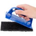A hand holding a blue Scrubble by ACS grill pad holder.