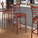 A group of Lancaster Table & Seating metal ladder back bar stools with mahogany wood grain finish and burgundy vinyl seats.