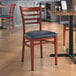 A Lancaster Table & Seating metal ladder back chair with mahogany wood grain finish and navy vinyl seat at a table in a restaurant.