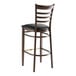 A Lancaster Table & Seating Spartan Series metal ladder back bar stool with dark walnut wood grain finish and black vinyl seat.