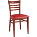 A Lancaster Table & Seating Spartan Series metal chair with mahogany wood grain finish and red vinyl cushion.