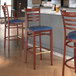 Three Lancaster Table & Seating metal ladder back bar stools with navy vinyl seats and mahogany wood grain finish.