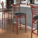 A group of Lancaster Table & Seating metal ladder back bar stools with mahogany wood grain finish and black vinyl seats next to a counter.