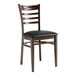 A Lancaster Table & Seating metal ladder back chair with dark walnut wood grain finish and black vinyl seat.