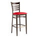A metal ladder back bar stool with a dark walnut wood grain finish and a red vinyl seat.