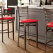 A metal bar stool with a dark walnut wood grain finish, ladder back design, and a red vinyl seat.