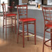 A Lancaster Table & Seating red metal bar stool with mahogany wood grain finish and red vinyl seat.