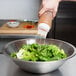 A hand using a Tablecraft SelecTop squeeze bottle to pour dressing onto a salad in a bowl.