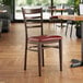 A Lancaster Table & Seating metal ladder back chair with dark walnut wood grain finish and burgundy vinyl seat.