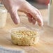 A clear 8 oz. round plastic deli container with a lid being placed on top, filled with macaroni salad.