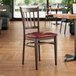 A Lancaster Table & Seating metal slat back chair with dark walnut wood grain finish and burgundy vinyl seat.