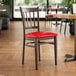 A Lancaster Table & Seating Spartan Series metal chair with dark walnut wood grain finish and a red vinyl seat.