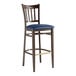 A Lancaster Table & Seating Spartan Series metal slat back bar stool with dark walnut wood grain finish and navy vinyl seat.