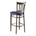 A Lancaster Table & Seating Spartan Series metal slat back bar stool with dark walnut wood grain finish and navy vinyl seat.