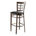 A Lancaster Table & Seating metal bar stool with black vinyl seat and wood grain finish.