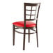 A Lancaster Table & Seating metal window back chair with dark walnut wood grain finish and red vinyl seat.