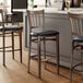 Three Lancaster Table & Seating Spartan Series metal slat back bar stools with black vinyl seats at a counter.
