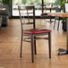 A Lancaster Table & Seating metal chair with dark walnut wood grain and a burgundy vinyl seat.